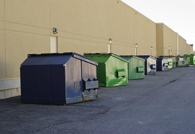 a construction worker unloading debris into a blue dumpster in Berlin, NY